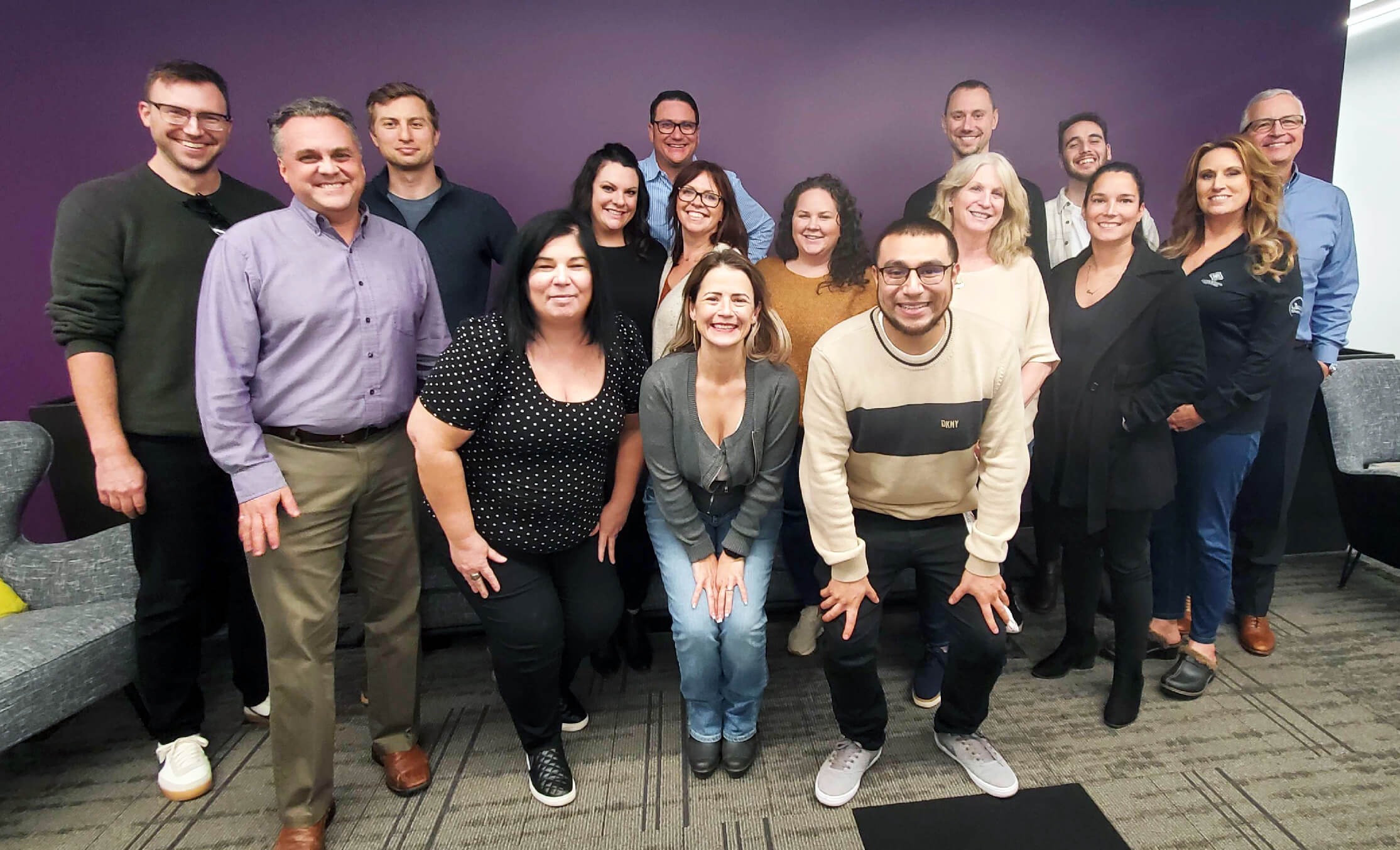 Team members posing in front of a purple wall